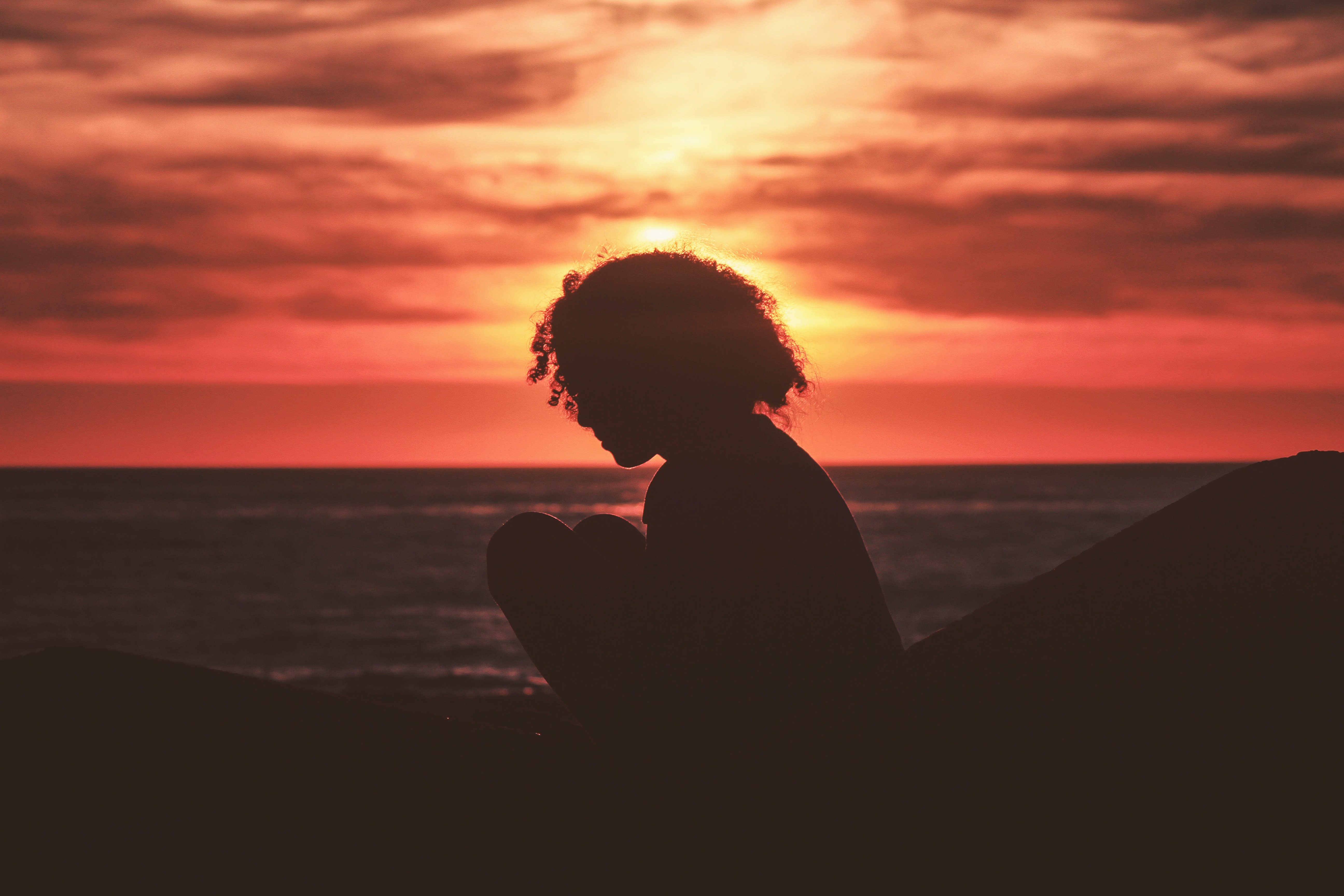 silhouette of girl sitting in front of sunset ocean